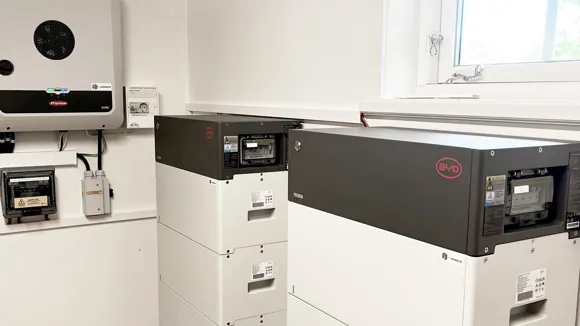 En växelriktare sitter på väggen och två batteristaplar står på golvet.