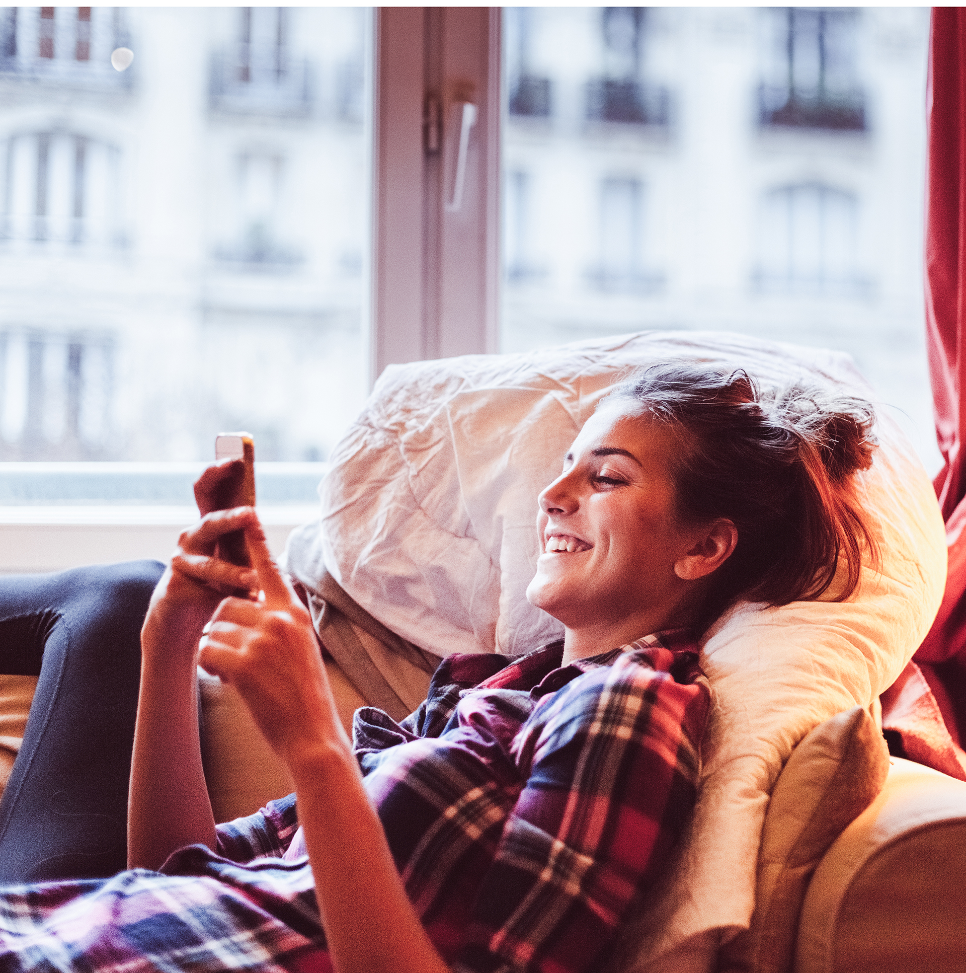 Foto av en leende kvinna som ligger i en soffa och tittar i sin mobiltelefon.