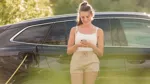 Kvinna laddar elbil och tittar i sin telefon utomhus.