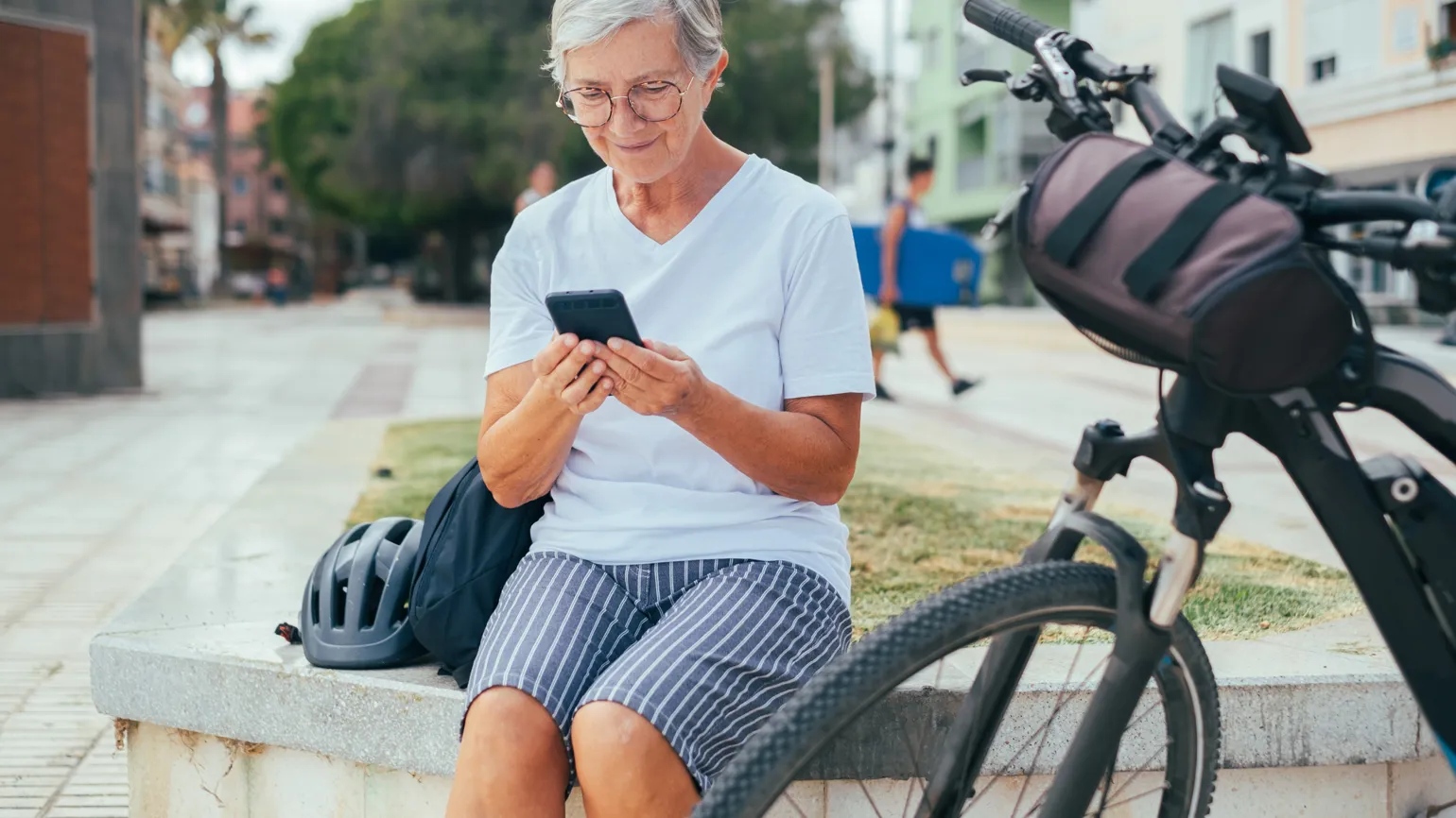 Kvinna tittar på mobilen sittandes bredvid en cykel.