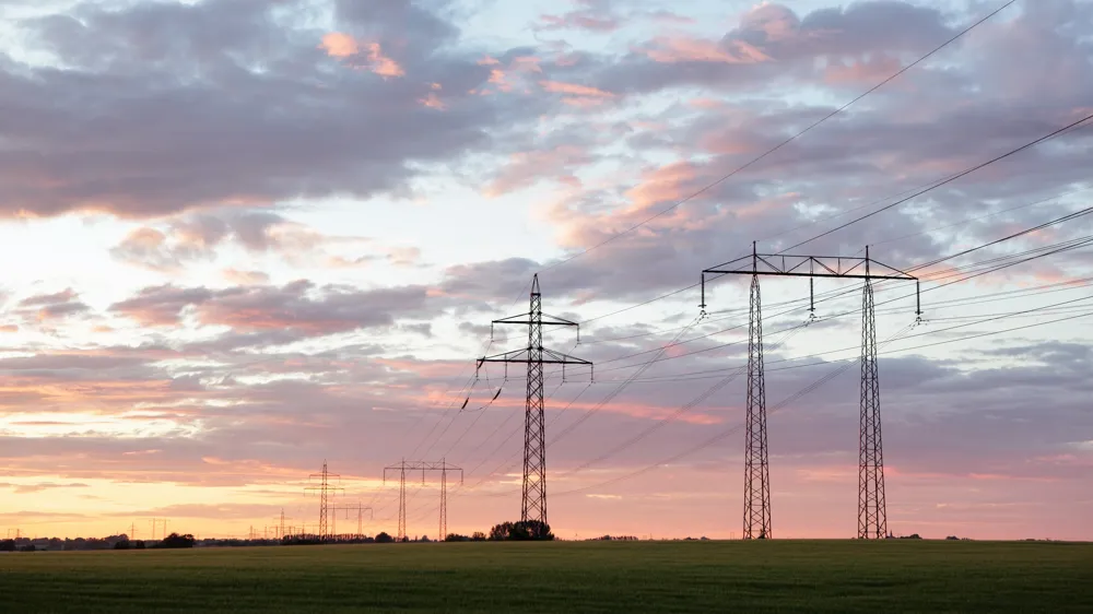 Kraftledningar över åker i skymningen. 