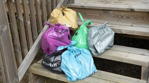 Fulla avfallspåsar i olika färger som står på en trappa utomhus.