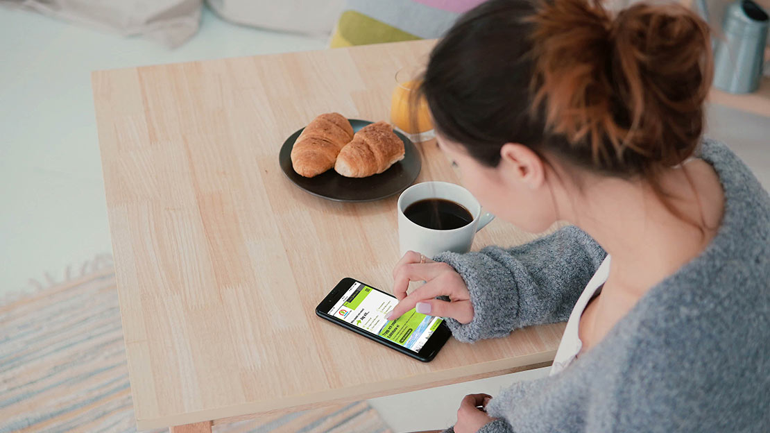 Kvinna skrollar på en mobil som ligger på ett bord.