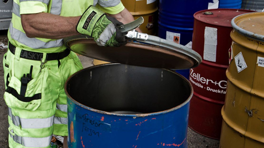 Person hanterar farligt avfall på fat.