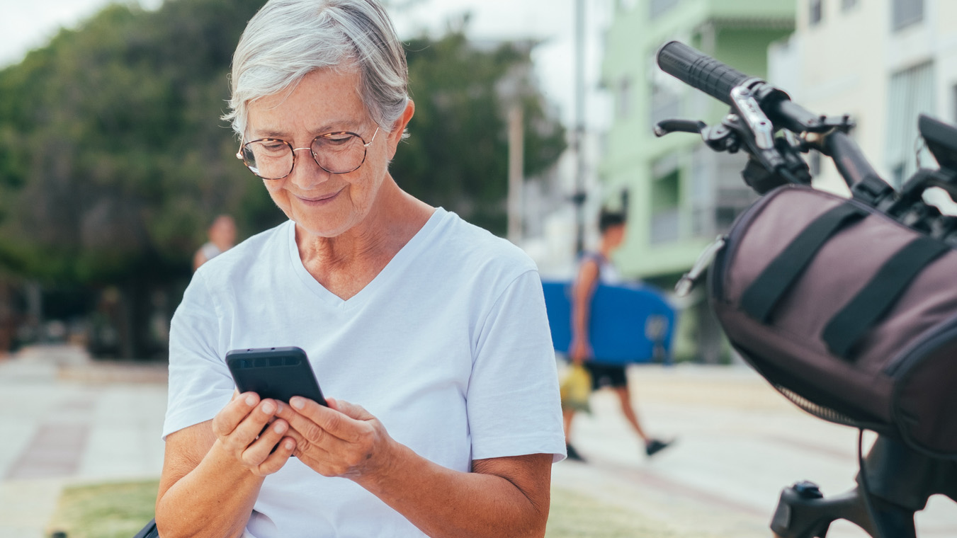 Äldre kvinna sittandes utomhus med en mobil.