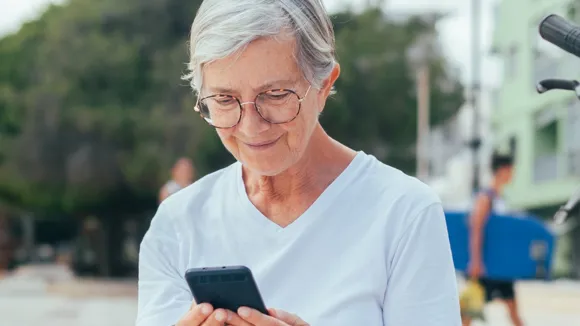 Äldre kvinna sittandes utomhus med en mobil.