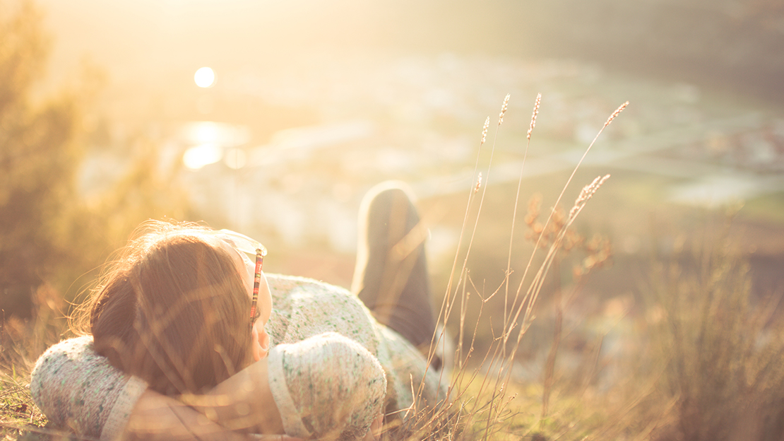 Kvinna liggandes på solig kulle.