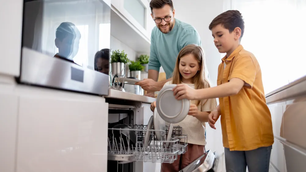 En pappa och två barn ställer in smutsig disk i diskmaskinen.
