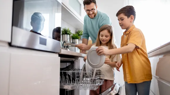 En pappa och två barn ställer in smutsig disk i diskmaskinen.