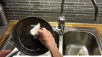 Hand torkar ur fett från stekpanna.
